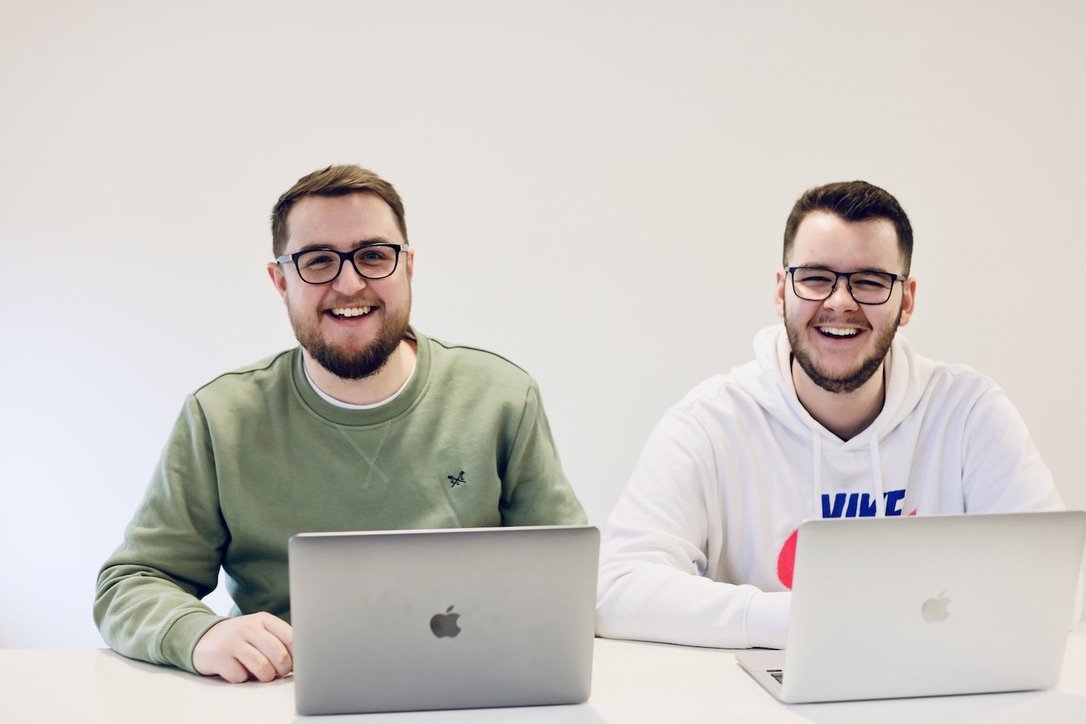 Two marketing and sales people working on laptops while laughing at the camera.