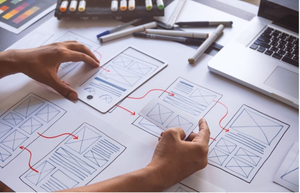 A designer art-boarding website design concepts using paper and card cutouts.