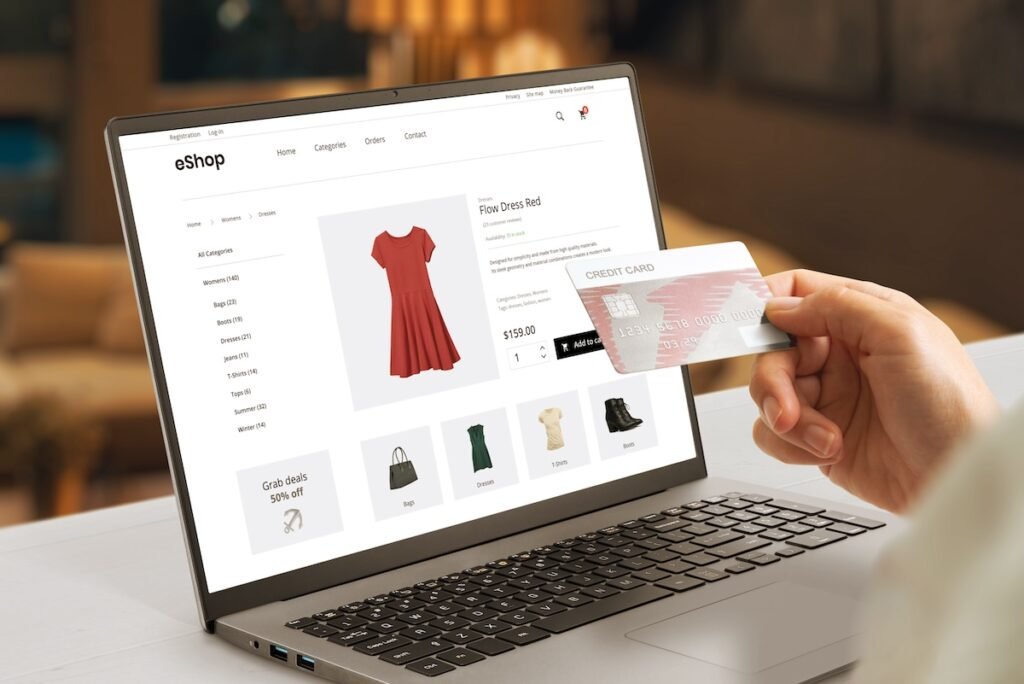A woman looking at buying a red dress on an ecommerce website on her laptop. She's holding her credit card up to read the numbers.