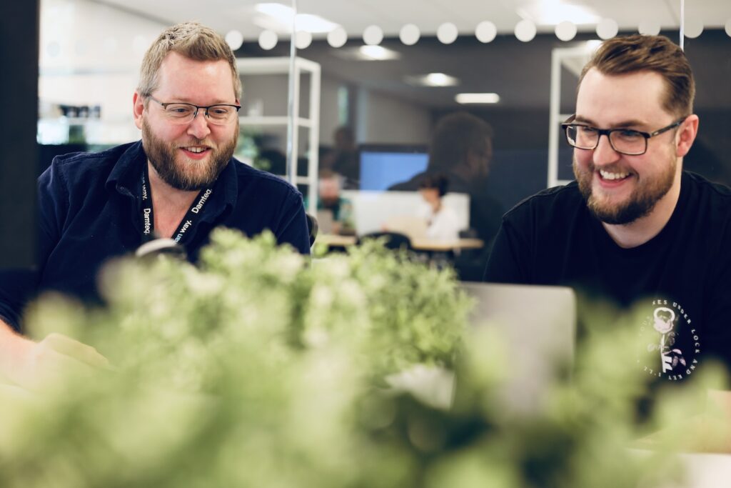 Two UX specialists working together in an office, smiling at their laptop.