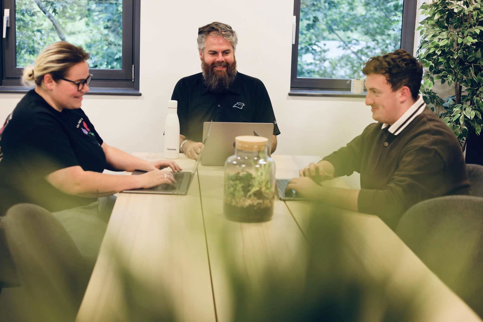 Three SEO specialists working collaboratively on their laptops at wooden table in a bright office.