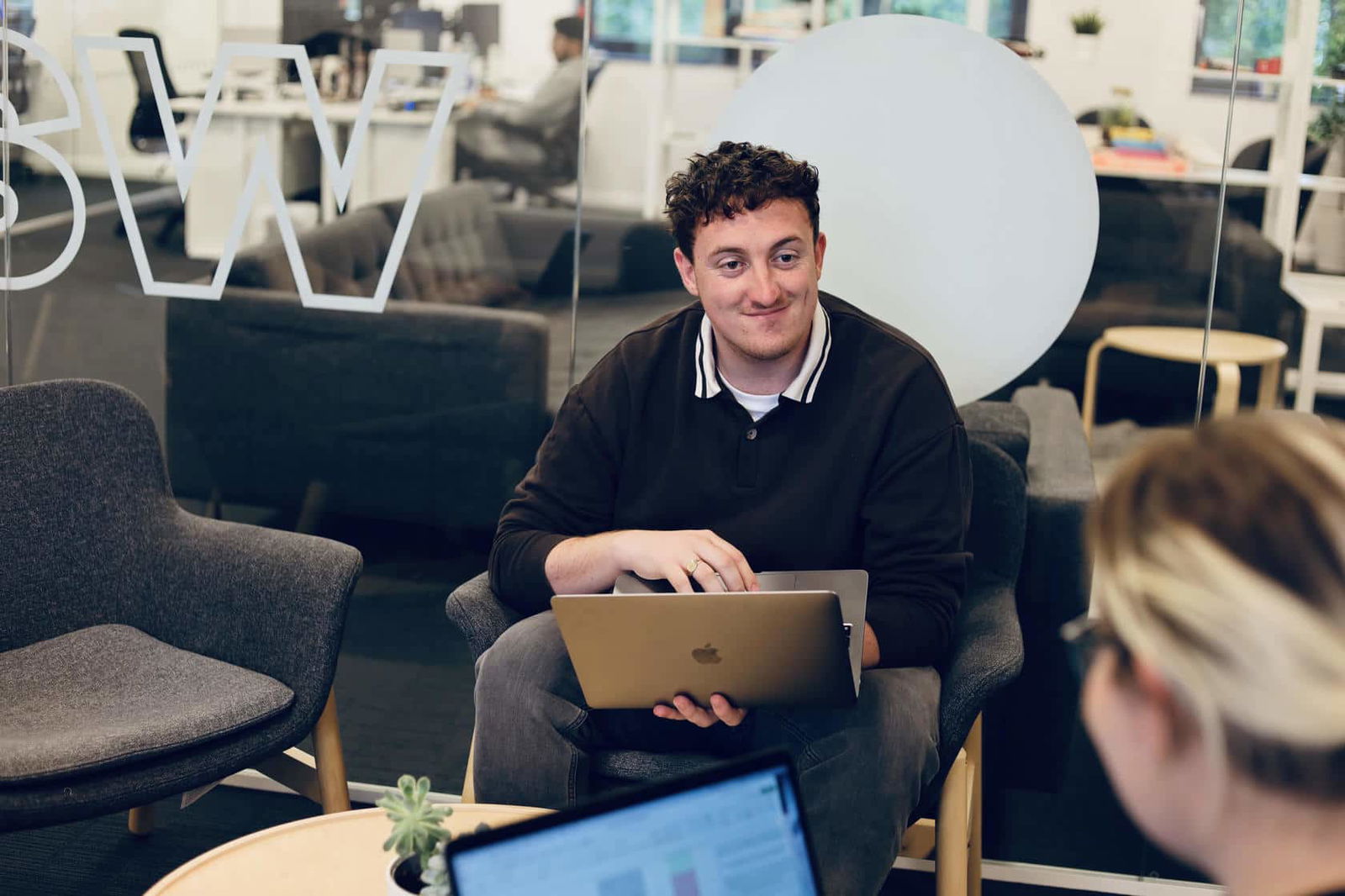 Will Wylde, one of Damteq's SEO specialists holding his laptop, while looking and smiling at one of his colleagues.