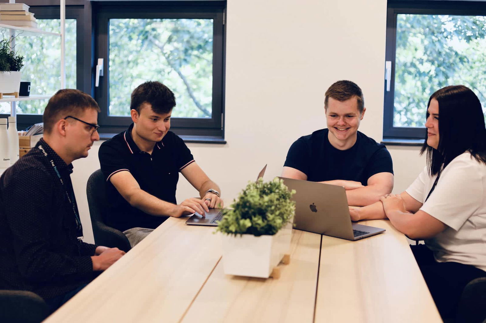 Damteq's PPC team having a group meeting on a wooden table in an office. They are all working on their laptops, and they have large windows behind them.