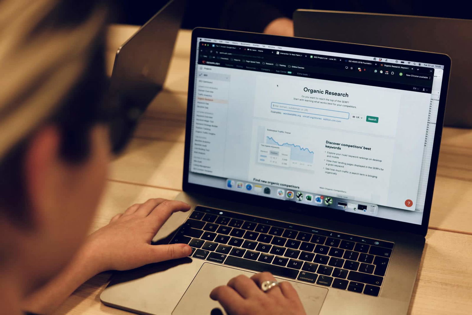 An SEO Specialist carrying out organic keyword research on her laptop at a wooden office table.